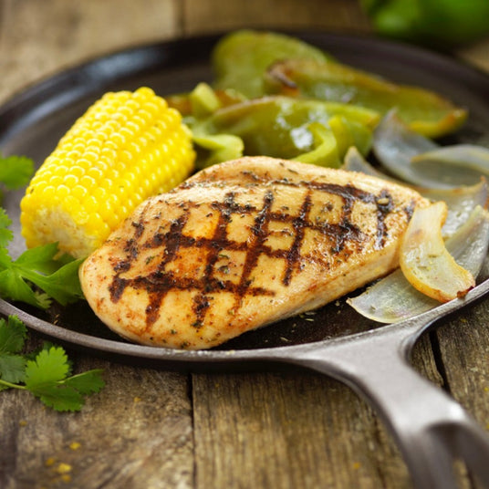 Halal Chicken breast with grill marks on a skillet served with corn on the cob and roasted onion and peppers