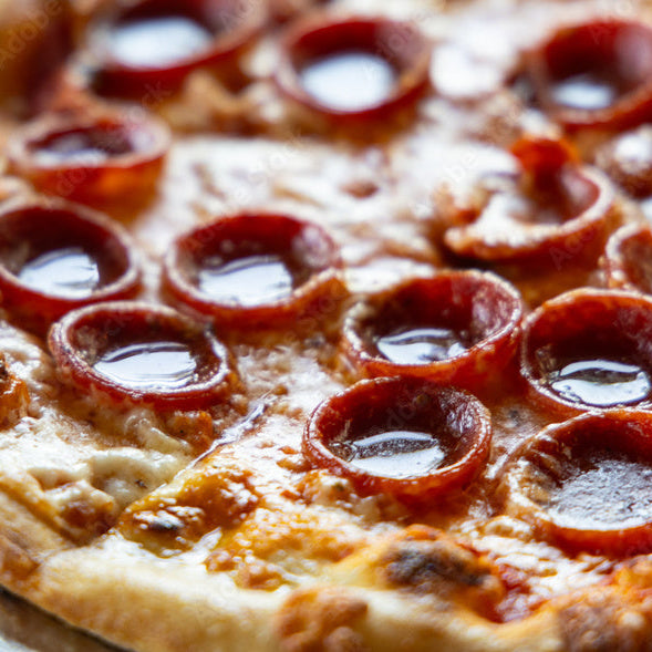 A close-up shot of a freshly baked pepperoni pizza on a metal pan, showing melted cheese and curled slices of pepperoni on a rustic wooden surface.