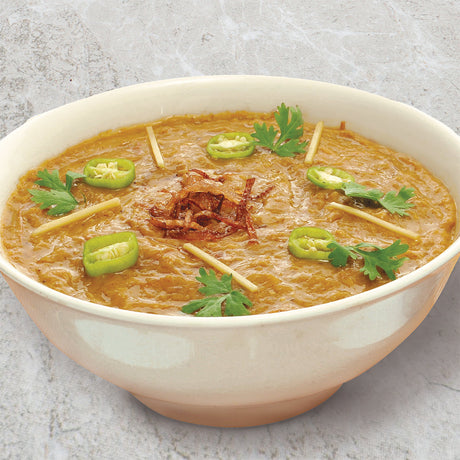 A white bowl filled with chicken Haleem with cilantro, sliced jalapeños, and fried onion on top.
