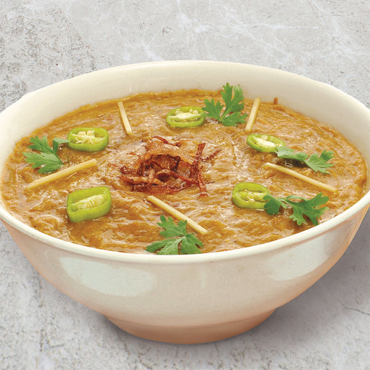 A white bowl filled with chicken Haleem with cilantro, sliced jalapeños, and fried onion on top.
