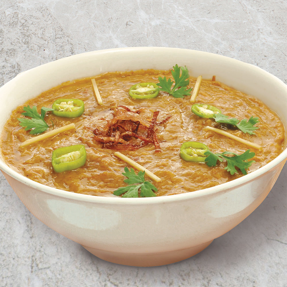 A white bowl filled with chicken Haleem with cilantro, sliced jalapeños, and fried onion on top.
