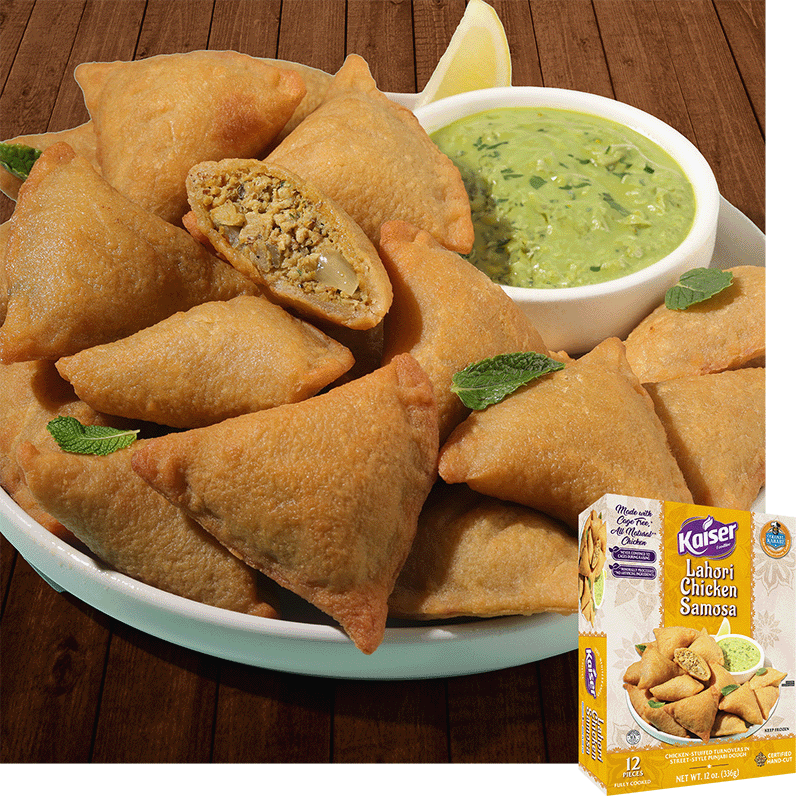 Kaiser Lahori Chicken Samosas in a pile on a white plate with some mint leaves. A bowl of chutney sits next to the pile. One samosa is cut in half and a minced meat mixture is visible inside. A package of Kaiser Lahori Chicken Samosa is overlaid in the bottom right corner.