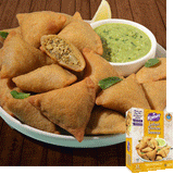 Kaiser Lahori Chicken Samosas in a pile on a white plate with some mint leaves. A bowl of chutney sits next to the pile. One samosa is cut in half and a minced meat mixture is visible inside. A package of Kaiser Lahori Chicken Samosa is overlaid in the bottom right corner.