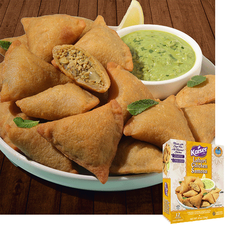 Kaiser Lahori Chicken Samosas in a pile on a white plate with some mint leaves. A bowl of chutney sits next to the pile. One samosa is cut in half and a minced meat mixture is visible inside. A package of Kaiser Lahori Chicken Samosa is overlaid in the bottom right corner.