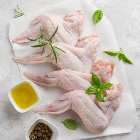 Raw chicken wings on a white plate with herbs and olive oil on a light gray background
