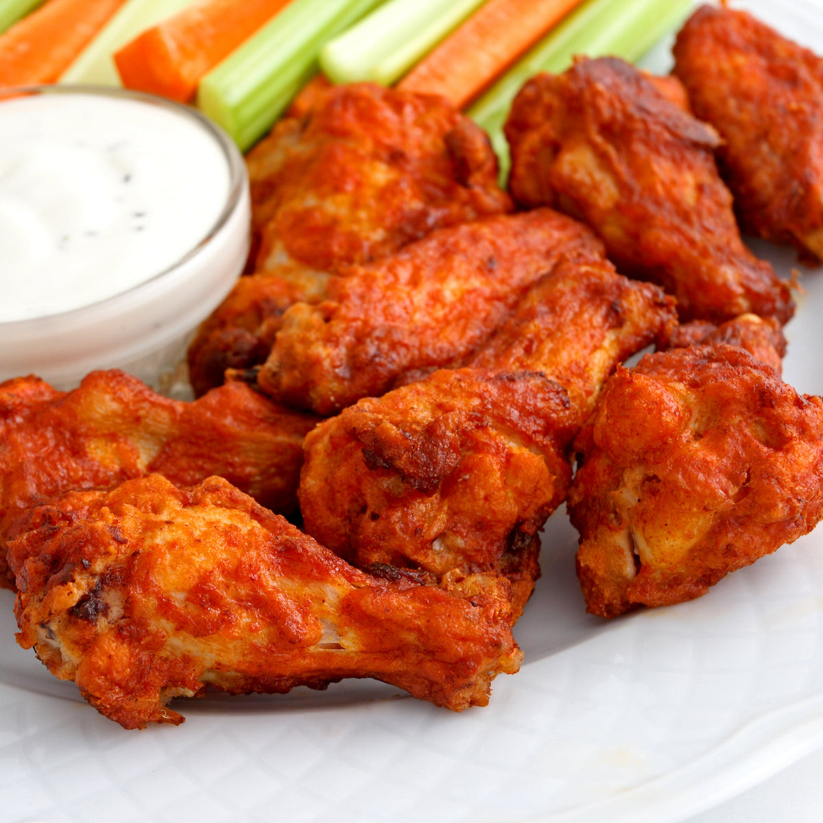 Baked chicken wings with a side of ranch dressing and vegetables on a white plate.